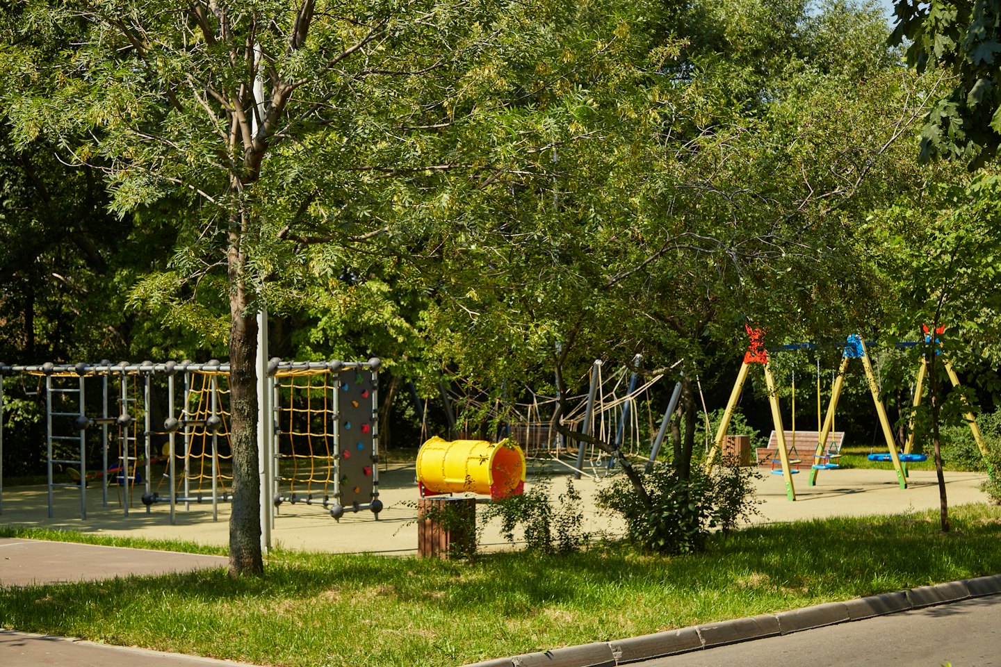 Bunte Spielplatzgeräte stehen auf einer grünen Parkwiese.