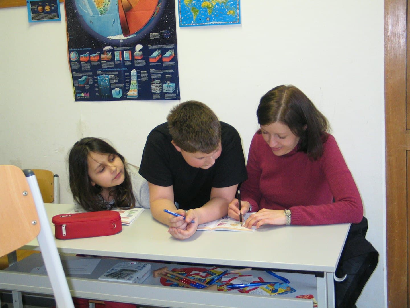 Lehrerin hilft zwei Kindern bei einer Aktivität am Schreibtisch.